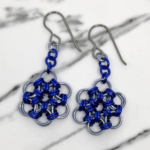 Könnte beinhalten: Ein Paar blaue und silberne Ohrringe in Blumenform. Die Ohrringe sind aus Metall und haben ein zartes, filigranes Design.