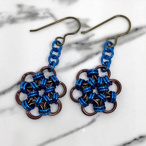 Könnte beinhalten: Ein Paar Ohrringe mit einem blauen und braunen Blumenmuster. Die Ohrringe sind aus Metall und haben einen Hakenverschluss.