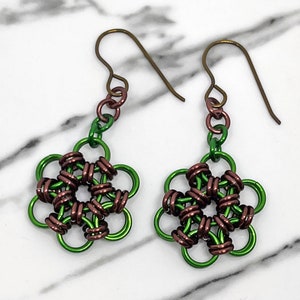 Könnte beinhalten: Ein Paar grüne und braune Drahtohhringe mit Blumenmuster. Die Ohrringe bestehen aus Draht, der zu einer Blumenform geflochten ist. Die Ohrringe hängen an einem einfachen Drahthaaken.