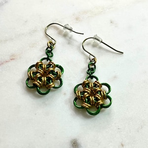 Könnte beinhalten: Ein Paar grüne und goldene Drahtohhringe mit einem Blumendesign. Die Ohrringe bestehen aus Draht, der verdreht und miteinander verwoben ist, um ein filigranes und komplexes Muster zu schaffen.