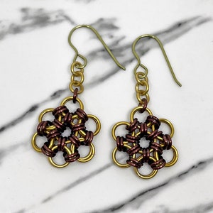 Könnte beinhalten: Ein Paar goldene und braune Ohrringe in Blumenform mit einem Kettenglieddesign. Die Ohrringe sind aus Metall und haben ein zartes, filigranes Design.