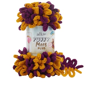Op de afbeelding: Een bol Alize Puffy More Plus garen in een paarse en gouden kleurcombinatie. Het garen zit in een verpakking met de merknaam en het garentype erop gedrukt.