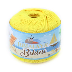 Op de afbeelding: Een heldergele bol Himalaya Bikini-garen. Het etiket toont een strandscène met een zeilboot, strandstoel en de merknaam. Ideaal voor het breien of haken van zomerkleding.