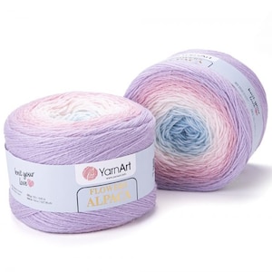 Może przedstawiać: Dwa motki włóczki w kolorze przechodzącym od różowego, przez biały do niebieskiego. Włóczka jest oznaczona jako "YarnArt Flower Alpaca".