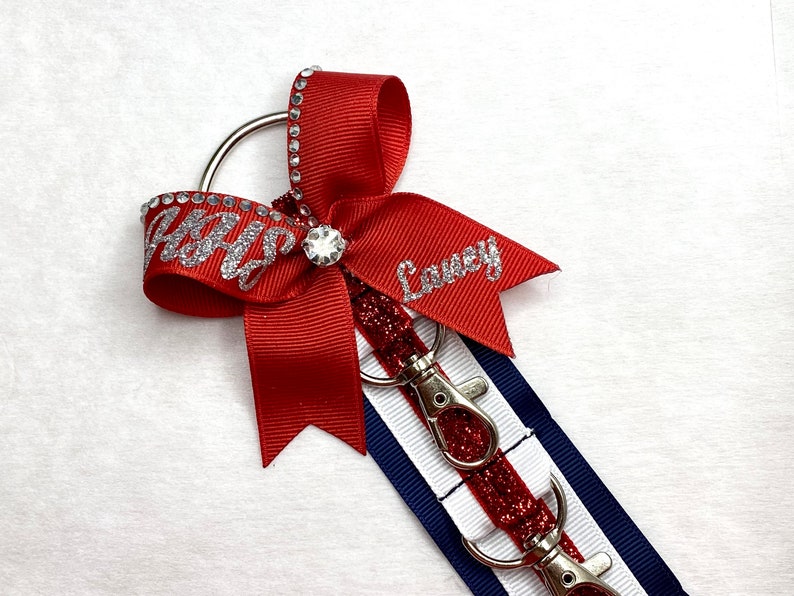 May include: Red, white, and blue ribbon with silver glitter lettering that says "Abby" and "Lovey". The ribbon is attached to a silver key chain with three silver key rings.