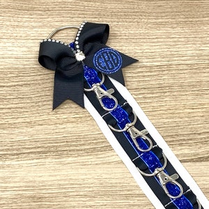 May include: A black and blue key chain with a black bow and a silver charm with a monogram. The key chain has five silver key rings.