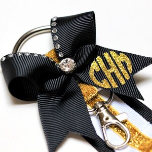 May include: Black and white ribbon keychain with a gold glitter ribbon and a gold glitter monogram "CHH". The keychain has a silver ring and a silver clip.