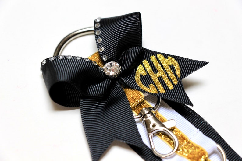 May include: Black and white ribbon keychain with a gold glitter ribbon and a gold glitter monogram "CHH". The keychain has a silver ring and a silver clip.