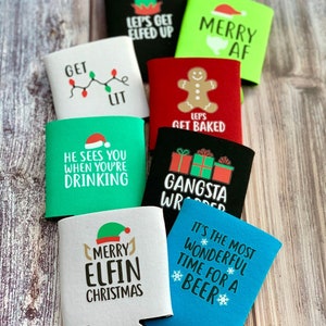 May include: A collection of ten Christmas-themed beverage insulators with various designs and sayings. The designs include a gingerbread man, a Christmas elf, a Christmas tree, and a Santa hat. The sayings include "Let's Get Elfed Up", "Merry AF", "Get Lit", "He Sees You When You're Drinking", "Let's Get Baked", "Gangsta Wrapper", "Merry Elfin Christmas", and "It's the Most Wonderful Time for a Beer".