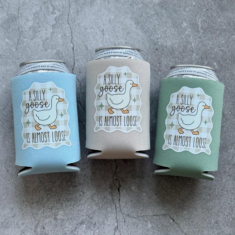 Op de afbeelding: Drie drankblikjeskoelers in lichtblauw, beige en groen. Elke koeler heeft een wit label met een cartoon gans en de tekst "A SILLY goose IS ALMOST LOOSE". De koelers zijn ontworpen om drankjes koud te houden.
