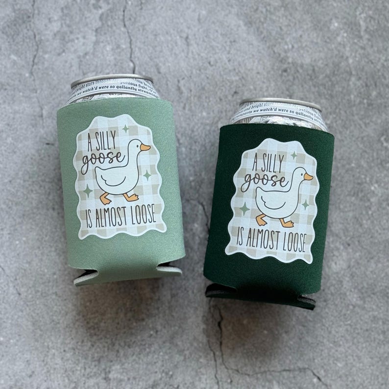 Op de afbeelding: Twee drankblikjeskoelers, &eacute;&eacute;n saliegroen en &eacute;&eacute;n donkergroen. Elk heeft een wit label met een cartoon gans en de tekst "A SILLY goose IS ALMOST LOOSE". De achtergrond is een grijs, getextureerd oppervlak.