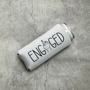May include: White can cooler with the word "ENGAGED" in black text and a black and white illustration of a hand giving the middle finger with pink nail polish.