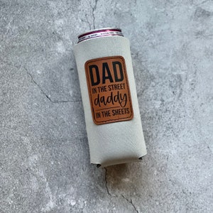 May include: A white neoprene can cooler with a brown leather patch that says "Dad in the street daddy in the sheets".