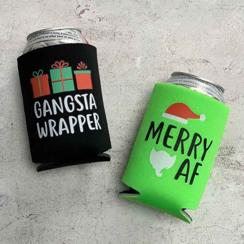 May include: Two black and green foam can coolers. One cooler has a red and green Christmas present design with the text "Gangsta Wrapper". The other cooler has a green background with a white Santa hat and the text "Merry AF".