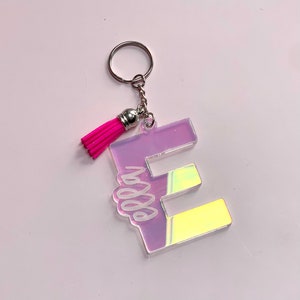 May include: A pink iridescent letter E keychain with a pink tassel. The letter E has the word "boss" written inside it.