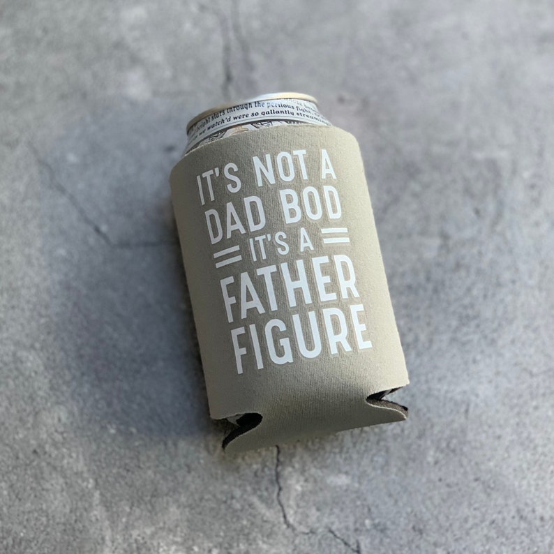 May include: A beige can cooler with the text "IT'S NOT A DAD BOD = IT'S A = FATHER FIGURE" in white.