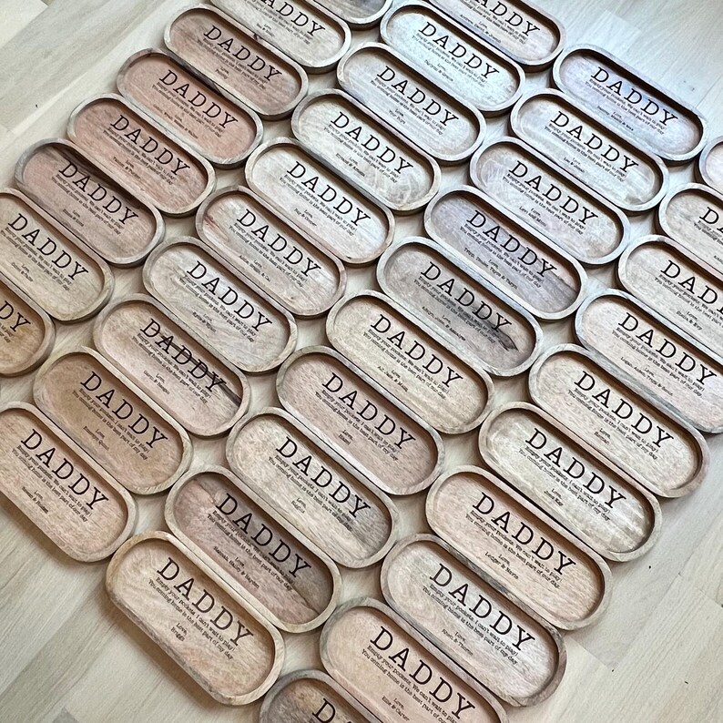 May include: A collection of wooden trays with the word "Daddy" engraved on them. Each tray has a different message about being a father.