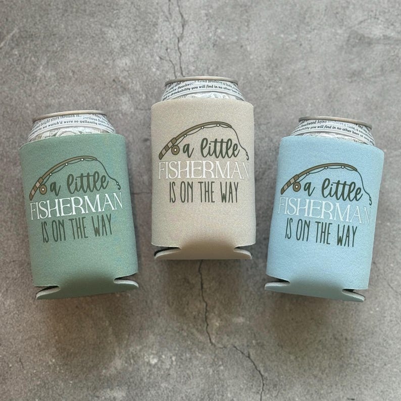 May include: Three different coloured can coolers with the text "a little fisherman is on the way" printed on them. The can coolers are green, beige, and blue.