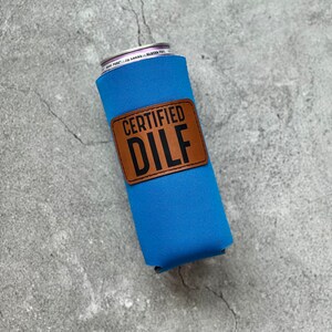 May include: A blue neoprene can cooler with a brown leather patch that says "CERTIFIED DILF" in black text.