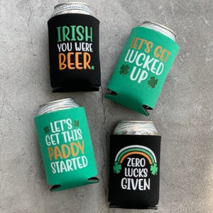 May include: Four green and black can coolers with St. Patrick's Day themed sayings. The sayings are "Irish You Were Beer", "Let's Get Lucked Up", "Let's Get This Paddy Started", and "Zero Lucks Given".