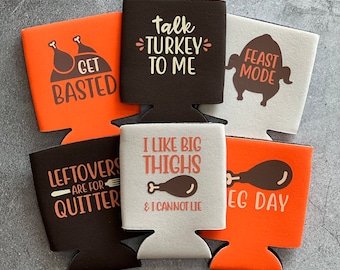 May include: Six different orange, brown, and white can coolers with Thanksgiving-themed sayings. The sayings include "Get Basted", "Talk Turkey To Me", "Feast Mode", "Leftovers Are For Quitters", "I Like Big Thighs & I Cannot Lie", and "Leg Day".