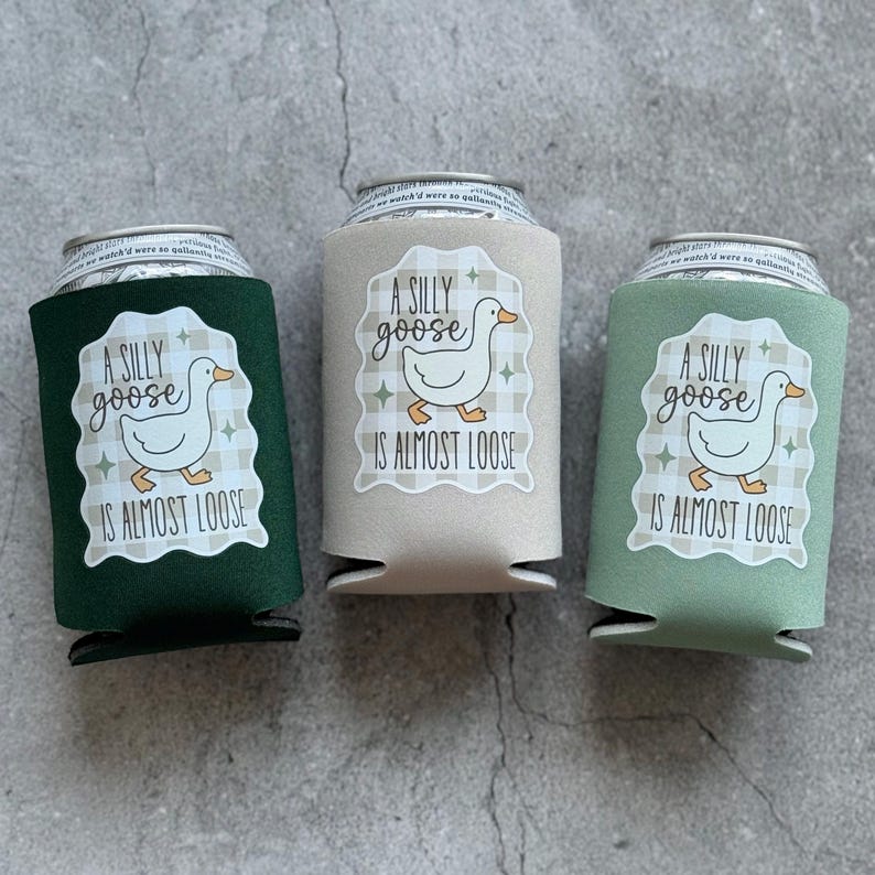 Op de afbeelding: Drie drankblikjeskoelers in groen, beige en saliegroen. Elke koeler heeft een wit label met een cartoon gans en de tekst "A SILLY goose IS ALMOST LOOSE". De koelers zijn ontworpen om drankjes koud te houden.