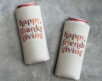 May include: Two beige can coolers with the phrases "happy thanks giving" and "happy friends giving" in a retro font. The text is in shades of brown and orange. The coolers are on a gray surface.