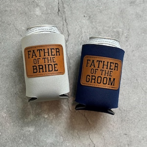 May include: Two can coolers, one light gray and one navy blue, each with a brown leatherette patch. The light gray cooler reads "FATHER OF THE BRIDE" and the navy blue cooler reads "FATHER OF THE GROOM".
