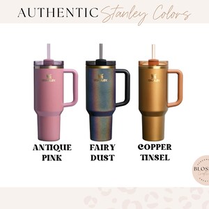 May include: Three Stanley tumblers with handles and straws, labeled Authentic Stanley Colors. The colors are Antique Pink, Fairy Dust, which is a dark iridescent finish, and Copper Tinsel. Each tumbler features the Stanley logo on the front.