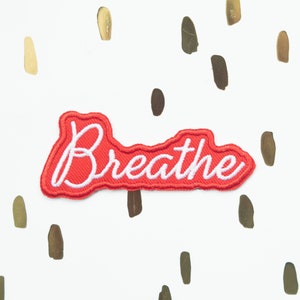Könnte beinhalten: Roter Filz-Patch mit weiß gesticktem Text "Breathe".
