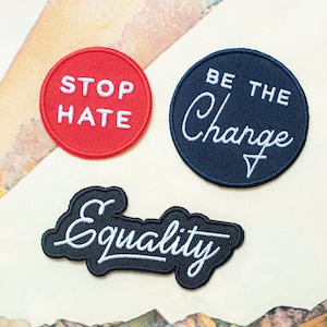 May include: Three embroidered iron-on patches with messages of social justice. The first patch is red with white text that says "Stop Hate". The second patch is black with white text that says "Be the Change". The third patch is black with white text that says "Equality".