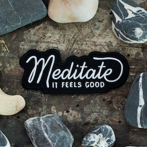 May include: Black and white embroidered patch with the text "Meditate It Feels Good" on a black background.