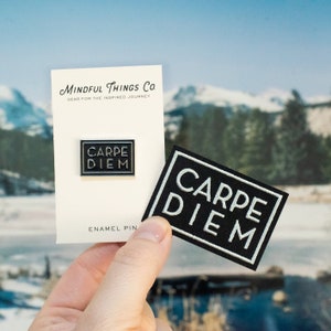 May include: A black enamel pin and a black patch with white text that reads "CARPE DIEM". The pin and patch are on a white card with the text "MINDFUL THINGS CO. GEAR FOR THE INSPIRED JOURNEY" and "ENAMEL PIN".