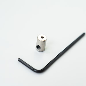 May include: A silver metal connector with a small hole in the center. A black metal hex wrench is also in the image.