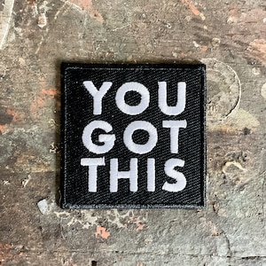 Może przedstawiać: Czarna łatka z tkaniny z białym haftem, na której widnieje napis "YOU GOT THIS".