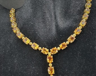 May include: A gold necklace with a pendant featuring a row of oval-shaped orange gemstones.