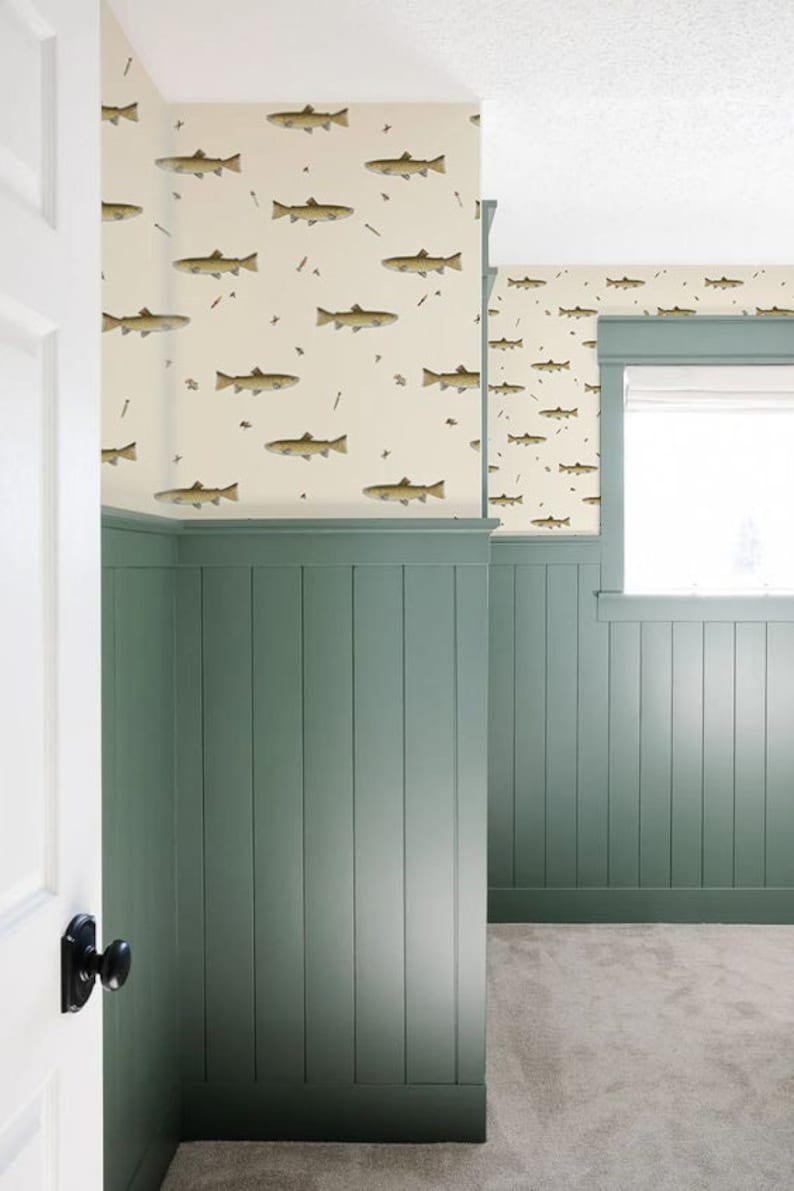 May include: A room with sage green wainscoting and a cream-colored wallpaper featuring a repeating pattern of fish. The room has a white door and a window with a white blind. The floor is covered in a light gray carpet.