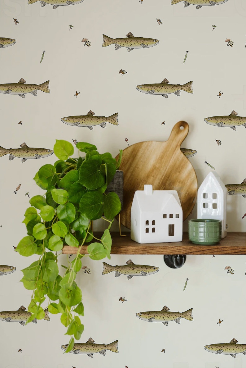 May include: A shelf with decorative items against a cream-colored wall with a fish pattern. Items include a wooden cutting board, white ceramic houses, a green plant, and a green ceramic pot.