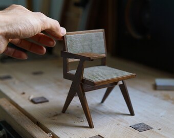 Könnte beinhalten: Ein Miniatur-Holzstuhl mit einem Stoffbezug und einer kleinen Armlehne. Der Stuhl ist aus dunklem Holz gefertigt und hat ein schlichtes, modernes Design.