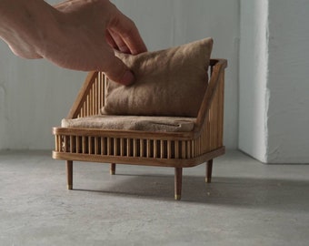 Könnte beinhalten: Ein Miniatur-Holzsessel mit einem braunen Kissen. Der Sessel hat eine Lattenrücklehne und -seiten, und das Kissen ist etwas größer als die Sitzfläche.