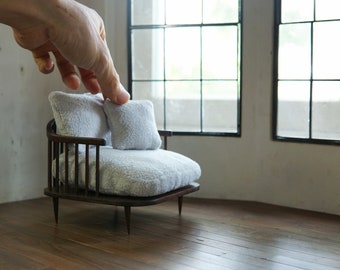 Könnte beinhalten: Ein weißer, gepolsterter Miniatur-Sessel mit zwei Kissen, aus Holz mit dunkelbrauner Oberfläche. Der Sessel steht auf einem Holzboden.