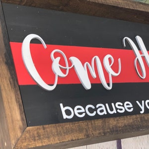 May include: Wooden sign with a red and black background. The sign says "Come Home because you are..." in white raised letters.