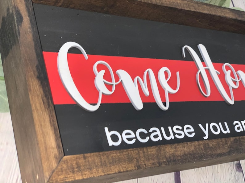 May include: Wooden sign with a red and black background. The sign says "Come Home because you are..." in white raised letters.
