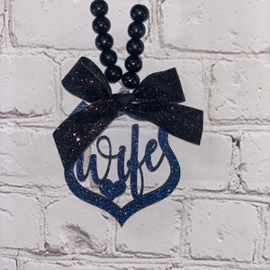 Pu&ograve; includere: Un ciondolo per auto in glitter blu e nero con la parola "moglie" in un design a forma di cuore. Il ciondolo &egrave; attaccato a una stringa di perline nere con un fiocco nero.