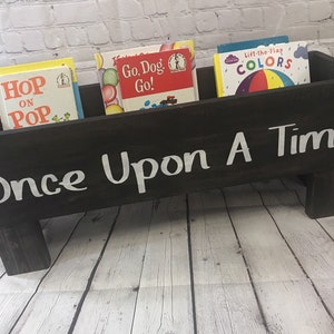 May include: A black wooden book bin with the words "Once Upon A Time" painted in white. The bin is filled with children's books, including "Hop on Pop", "Go, Dog, Go!" and "Lift-the-Flap Colors".