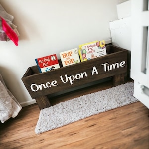 May include: A wooden book shelf with the words "Once Upon A Time" painted on the front. The shelf is filled with children's books, including "Go Dog Go!" "Hop On Pop" and "If You Give A Pig A Party".