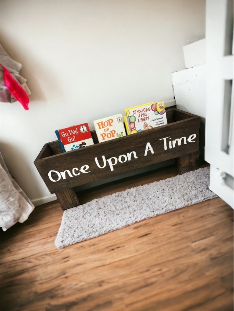 May include: A wooden book shelf with the words "Once Upon A Time" painted on the front. The shelf is filled with children's books, including "Go Dog Go!" "Hop On Pop" and "If You Give A Pig A Party".