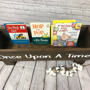 May include: A wooden book bin with the words "Once Upon A Time" painted on the front. The bin is filled with three children's books: "Go, Dog. Go!" by P.D. Eastman, "Hop on Pop" by Dr. Seuss, and "If You Give a Pig a Party" by Laura Numeroff and Felicia Bond.