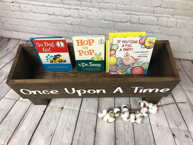 May include: A wooden book bin with the words "Once Upon A Time" painted on the front. The bin is filled with three children's books: "Go, Dog. Go!" by P.D. Eastman, "Hop on Pop" by Dr. Seuss, and "If You Give a Pig a Party" by Laura Numeroff and Felicia Bond.