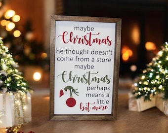 May include: A wooden sign with a white background and brown frame. The sign features a green Grinch hand holding a red ornament and the text "maybe Christmas he thought doesn't come from a store maybe Christmas perhaps means a little bit more".
